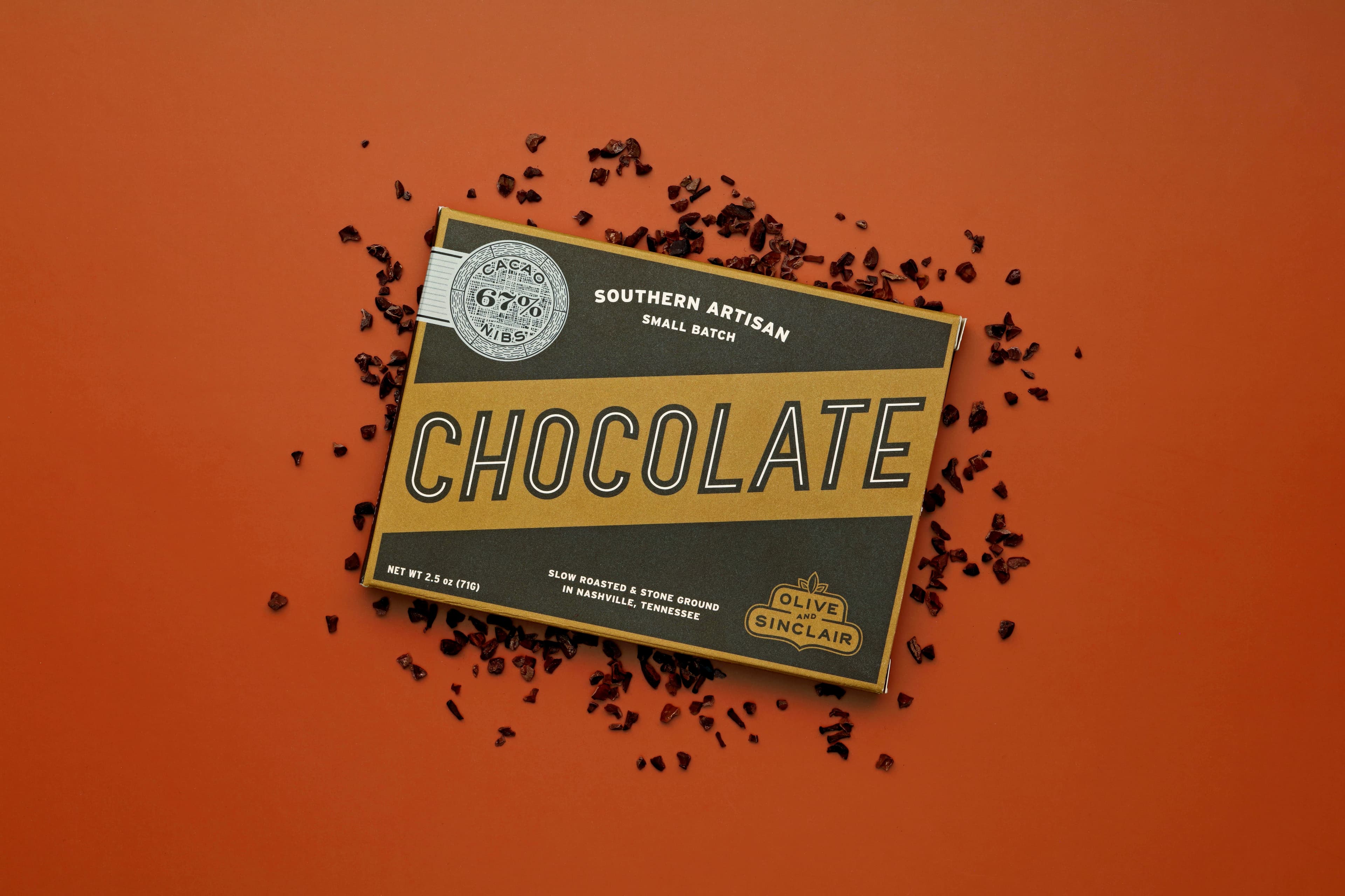 67% Cacao Nibs bar made by Olive & Sinclair Chocolate Co in the United States on an orange backgorund with cacao nibs scattered around