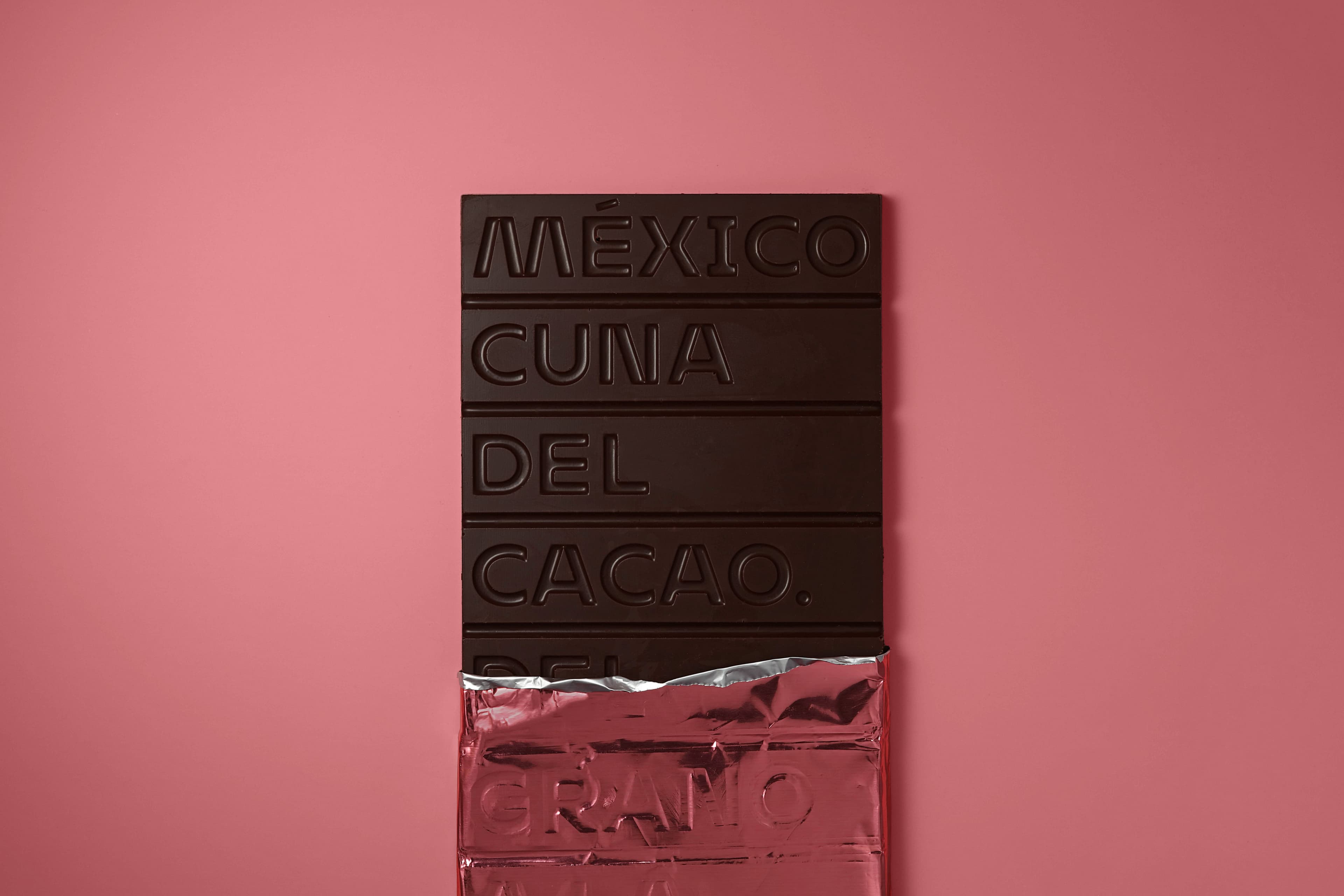73% MEXICAN CACAO from Soconusco, Chiapas with Mezcal Joven bar made by CUNA DE PIEDRA in Mexico with with the pink foil packaging torn on a pink background