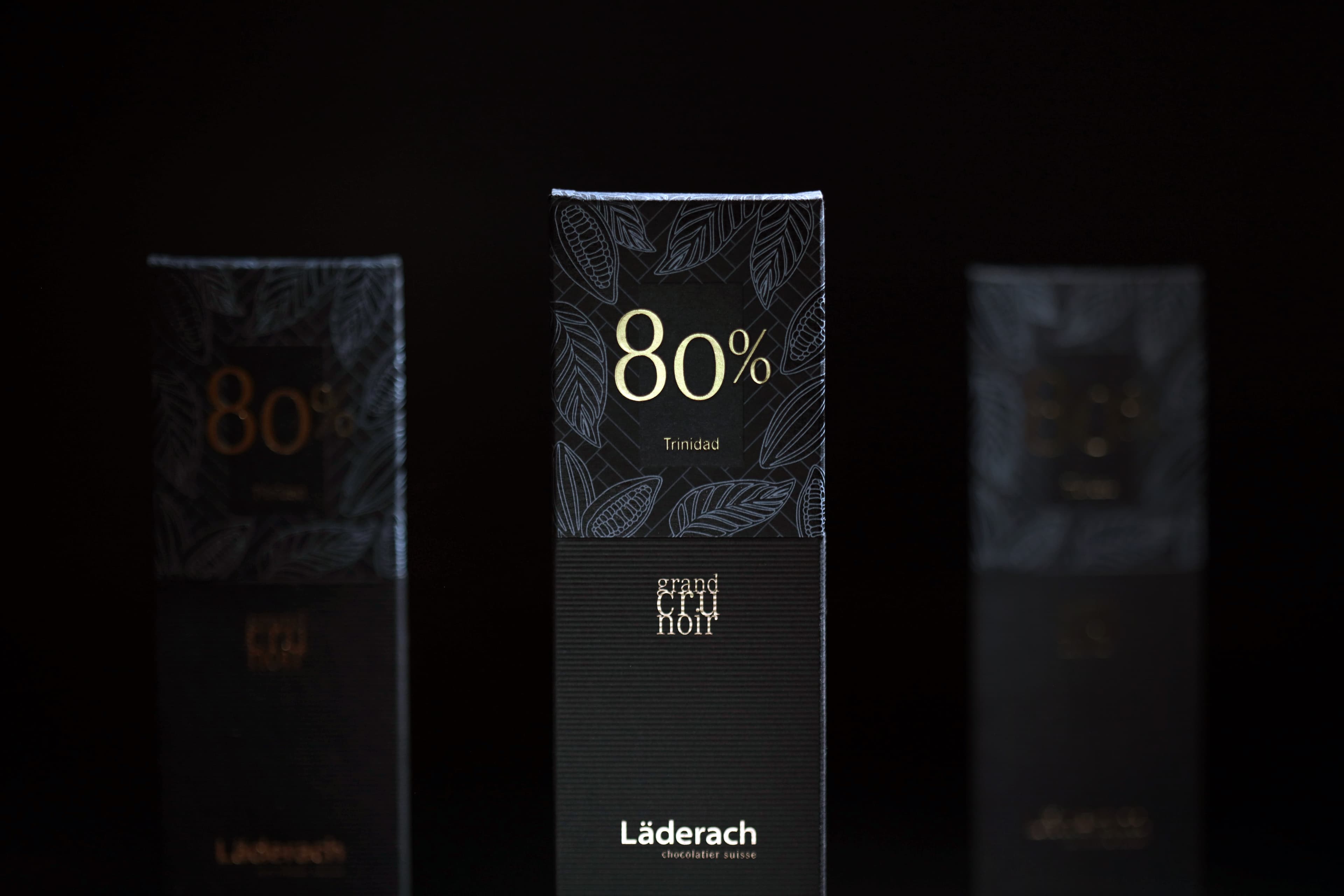 80% Trinidad Grand Cru Noir bar made by Laderach in Switzerland centered in a moody scene with bars out of focus on the left and right
