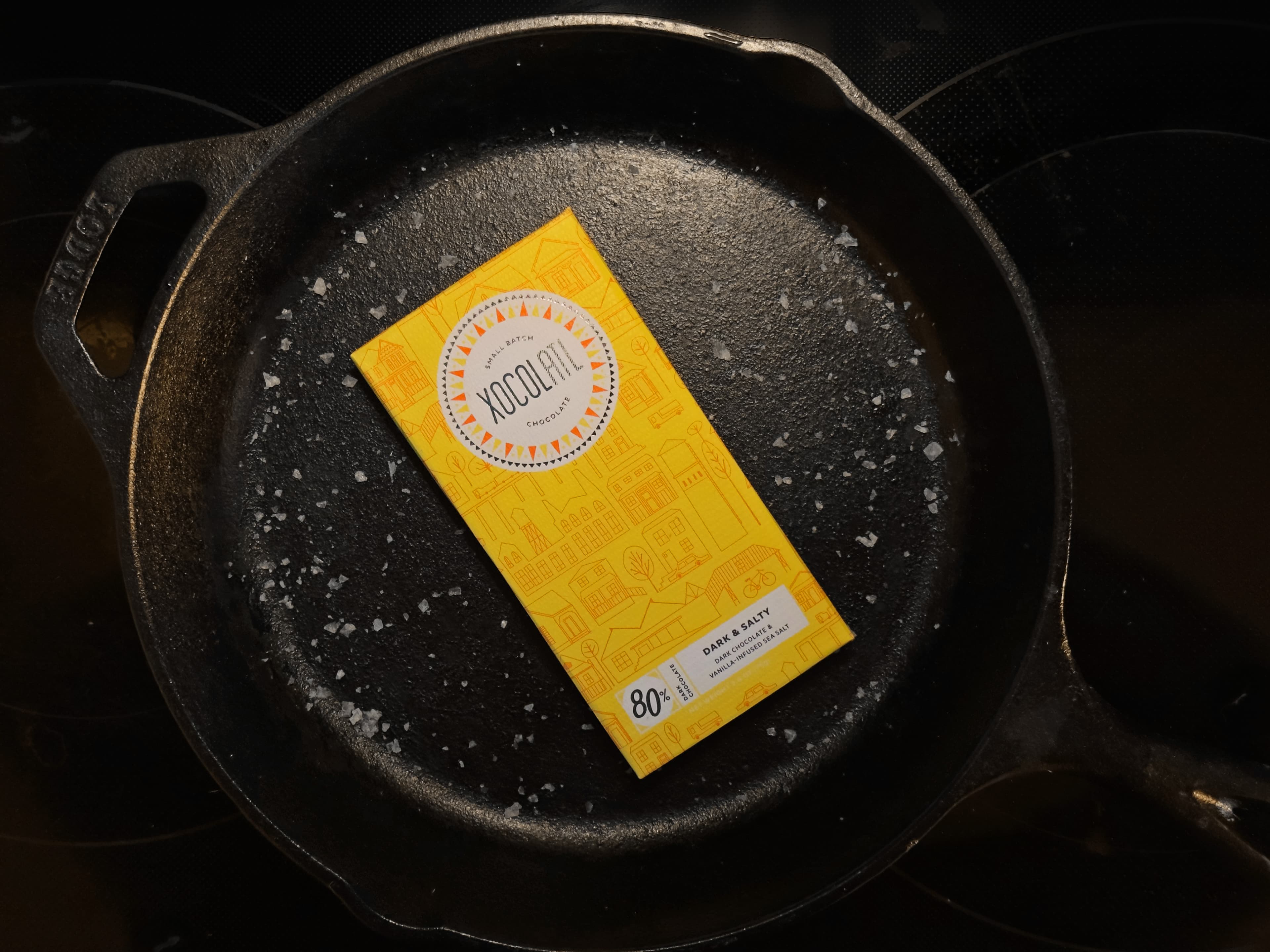 Dark & Salty Dark Chocolate & Vanilla-Infused Sea Salt bar from Xocolatl Small Batch Chocolate in cast iron pan with salt