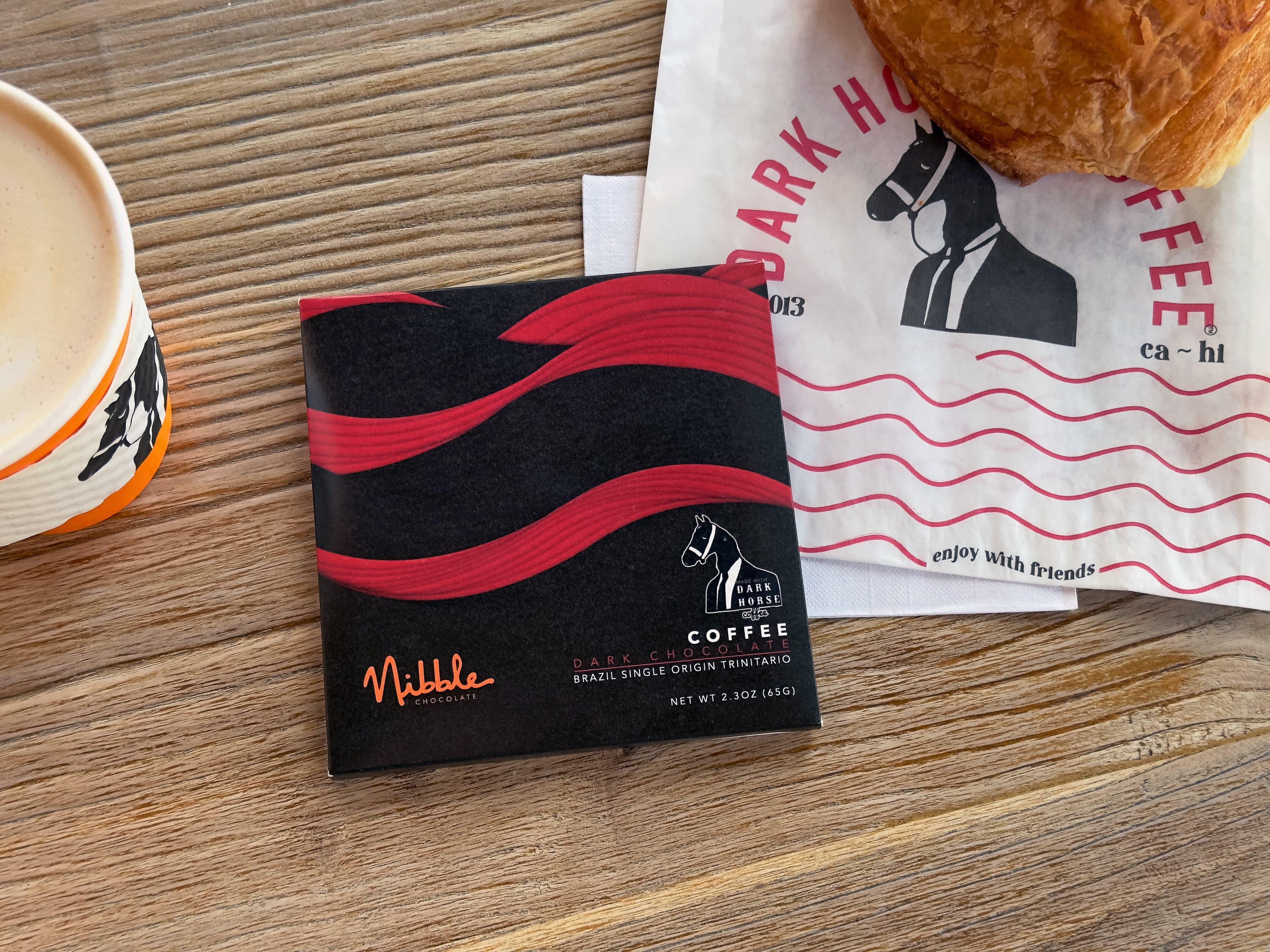 Dark Horse Coffee Dark Chocolate bar made by Nibble Chocolate in the United States on a table with dark horse coffee and a pastry