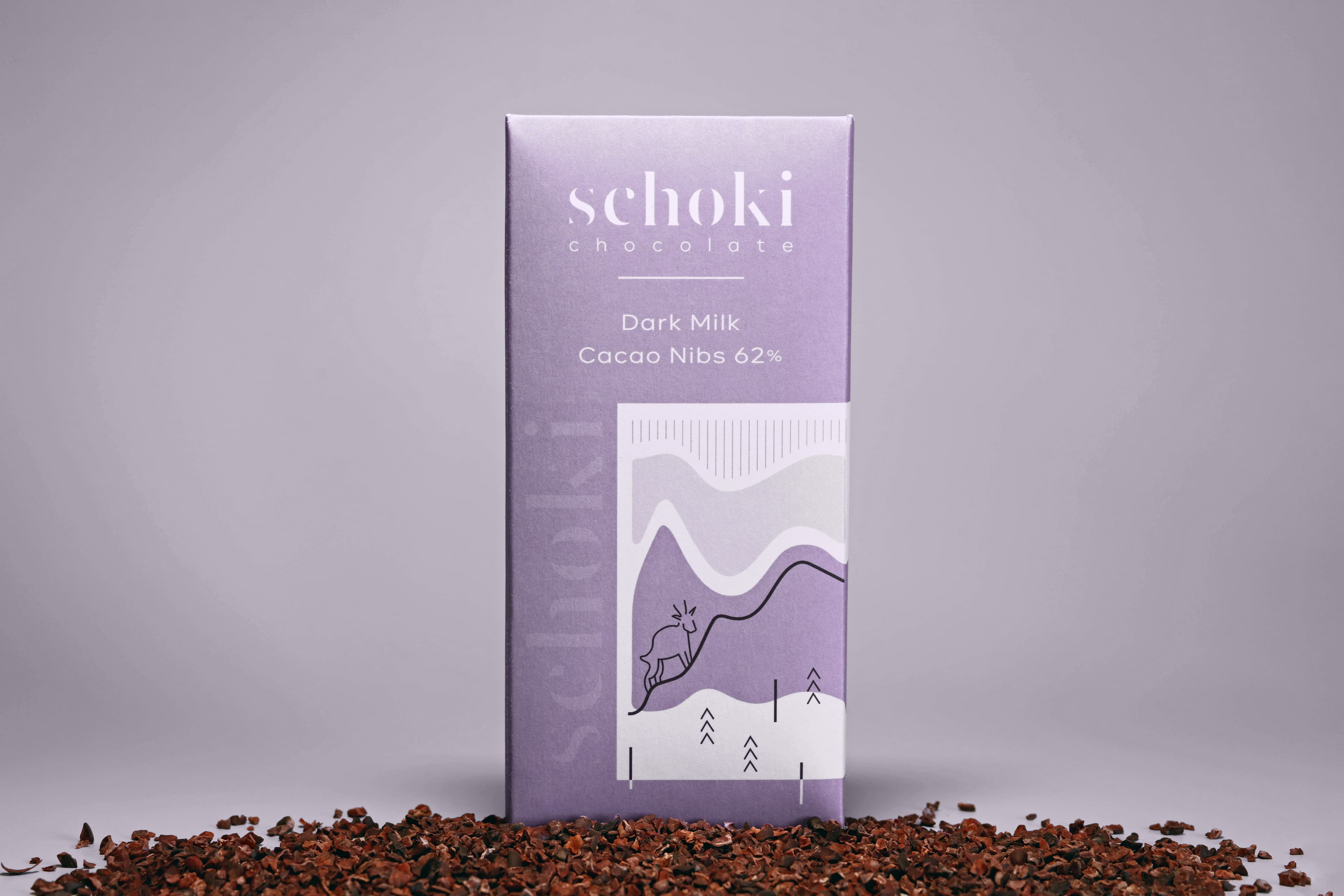 Dark Milk Cacao Nibs 62% bar made by Schoki Chocolate in Canada with standing in a pile of cacao nibs