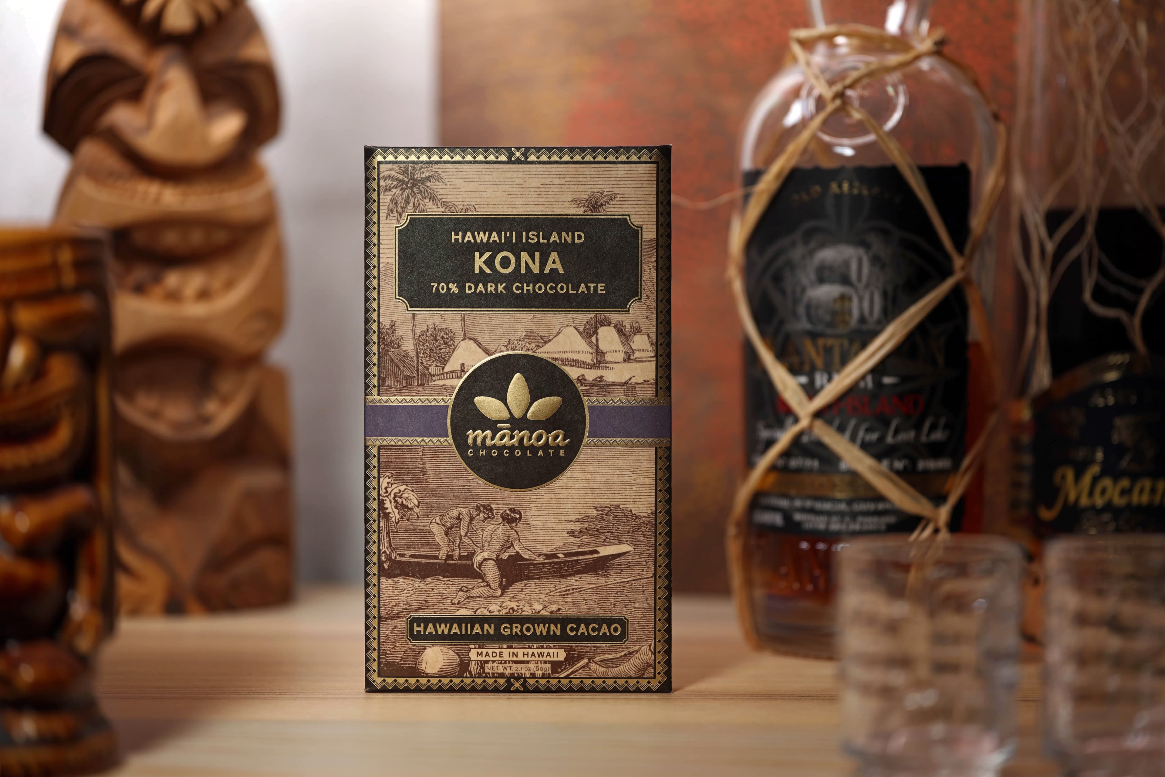 Kona Hawai'i Island 70% Dark Chocolate bar made by Manoa Chocolate in the United States in a tikibar scene with rum and carved wood heads