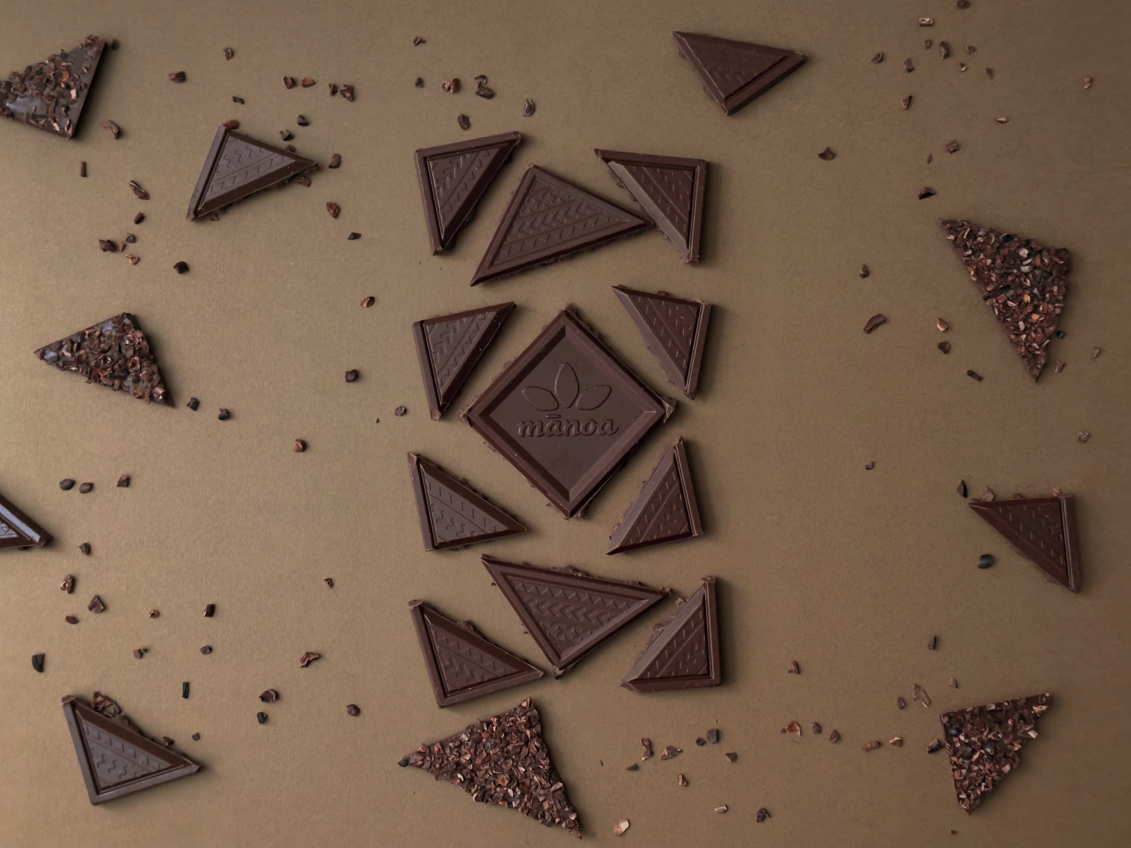 Kope Coffee 60% Dark Milk Chocolate & Nibs bar from Manoa Chocolate exploded with nibs on a brown background