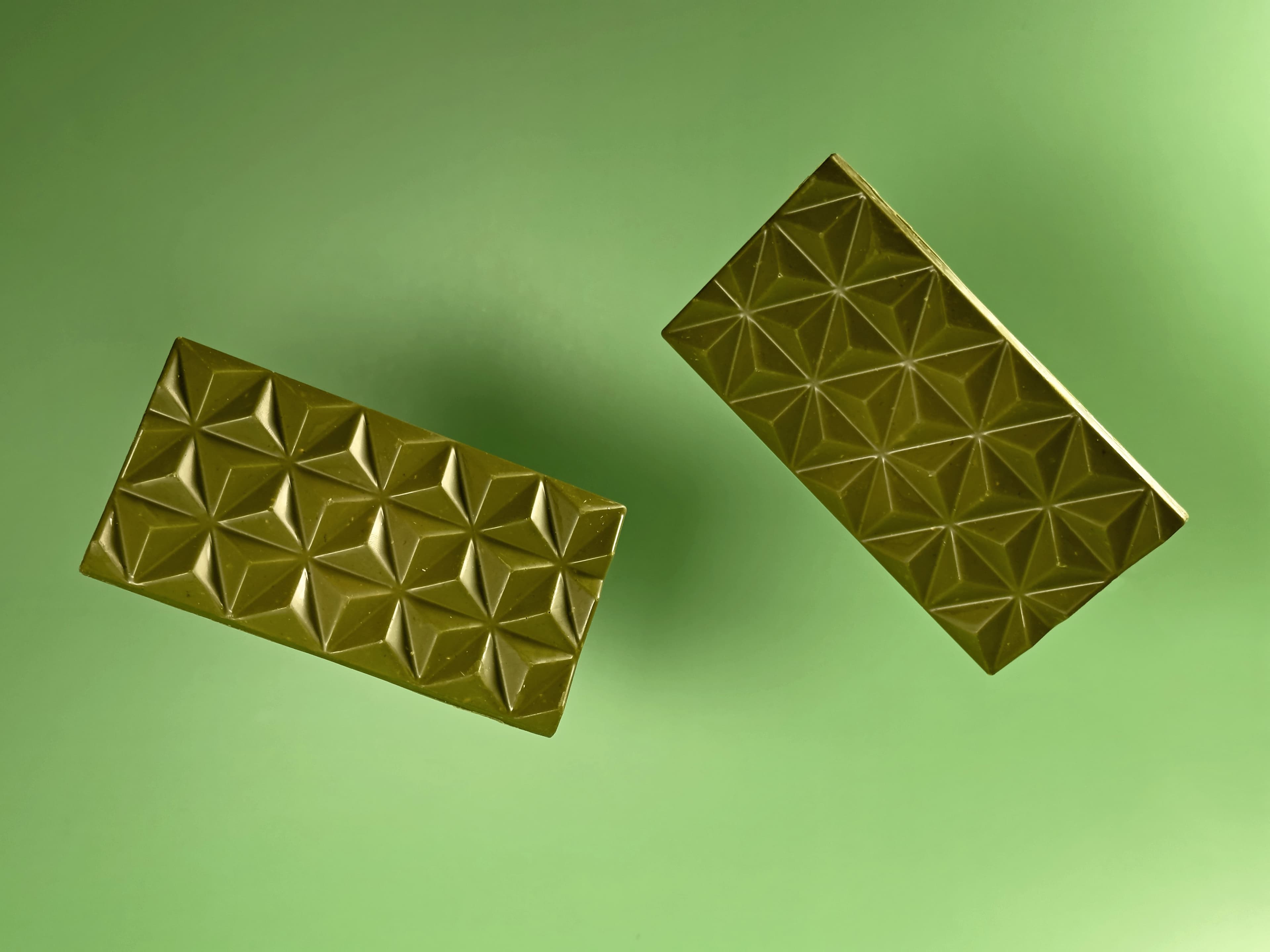 Pair of Matcha Chocolate with Caramelized Sesame bars made by Deux Cranes floating on a green background
