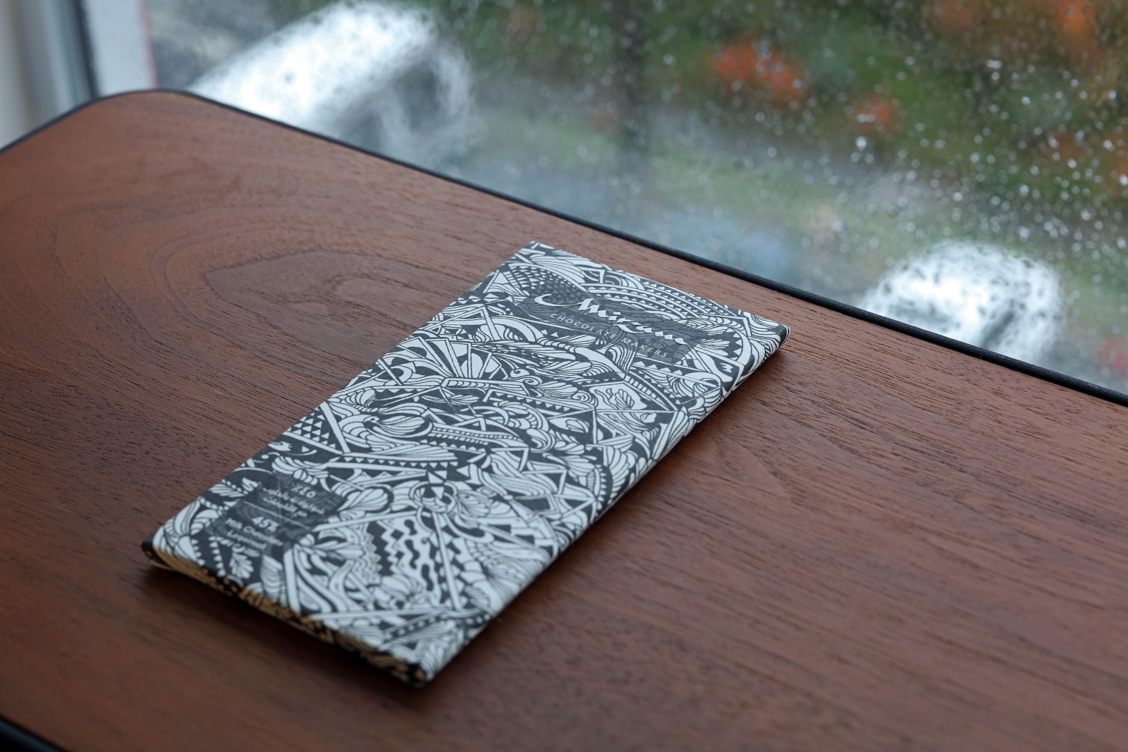 Milk Chocolate with Loqaimat bar made by Mirzam Chocolate Makers in United Arab Emirates on a side table with rain outside the window