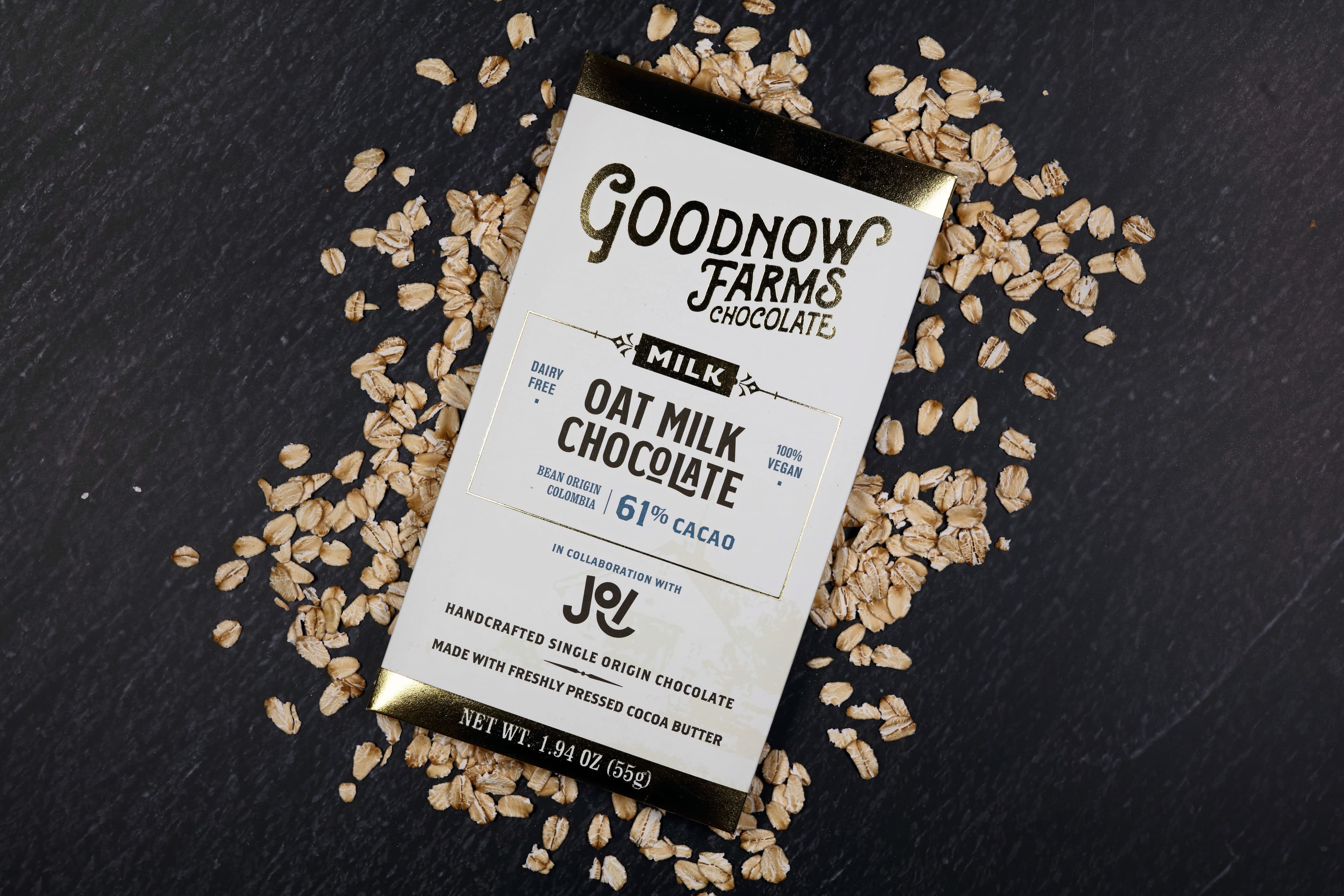 Oat Milk Chocolate 61% Cacao bar made by Goodnow Farms Chocolate in the United States on a dark background with oats scattered bedhind it in an artful manner