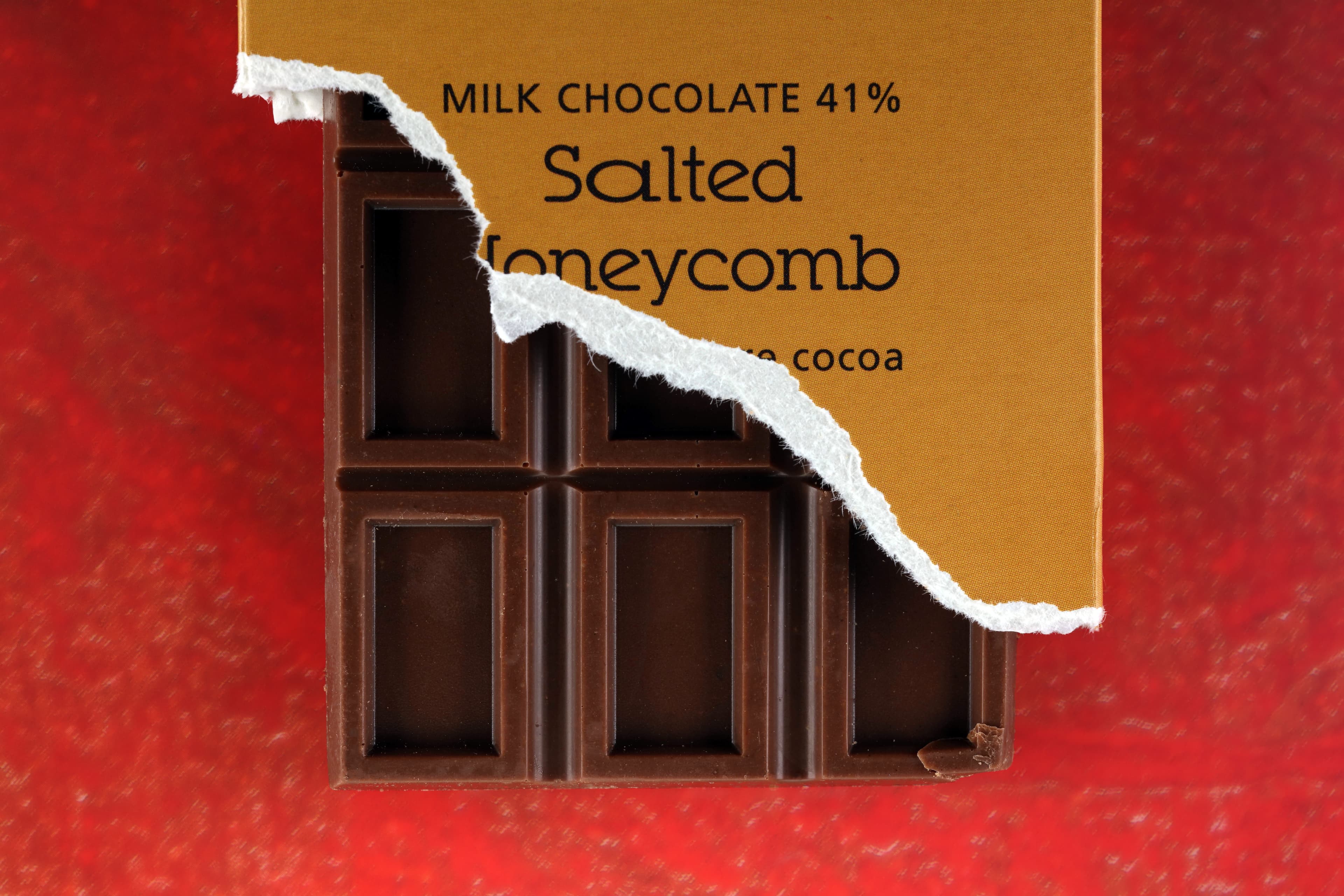 Salted Honeycomb Milk Chocolate 41% bar made by Artisan du Chocolat in England macro shot with the box torn and the bar sticking out