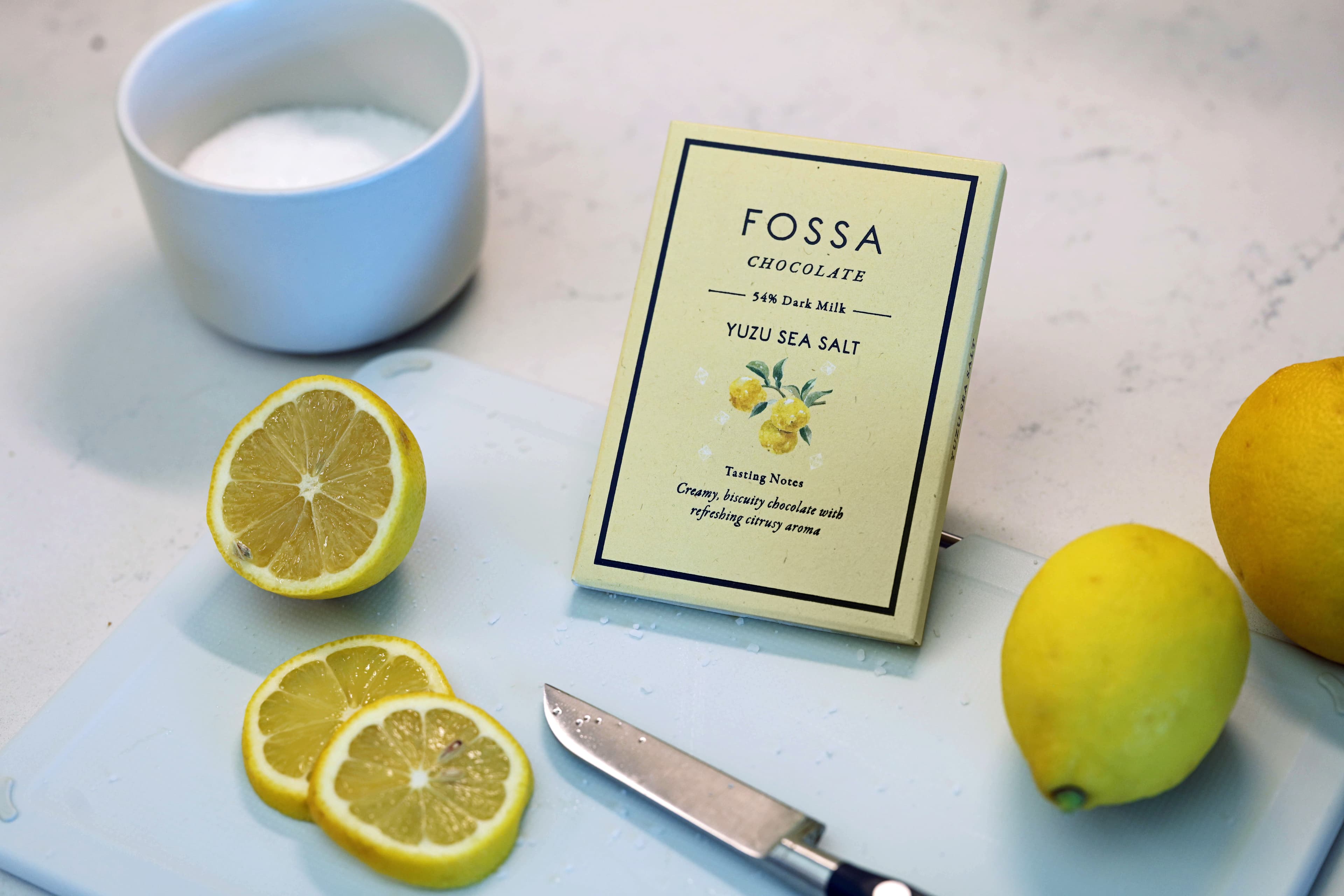 Yuzu Sea Salt bar made by Fossa Chocolate in Singapore on a cutting board with lemons and salt