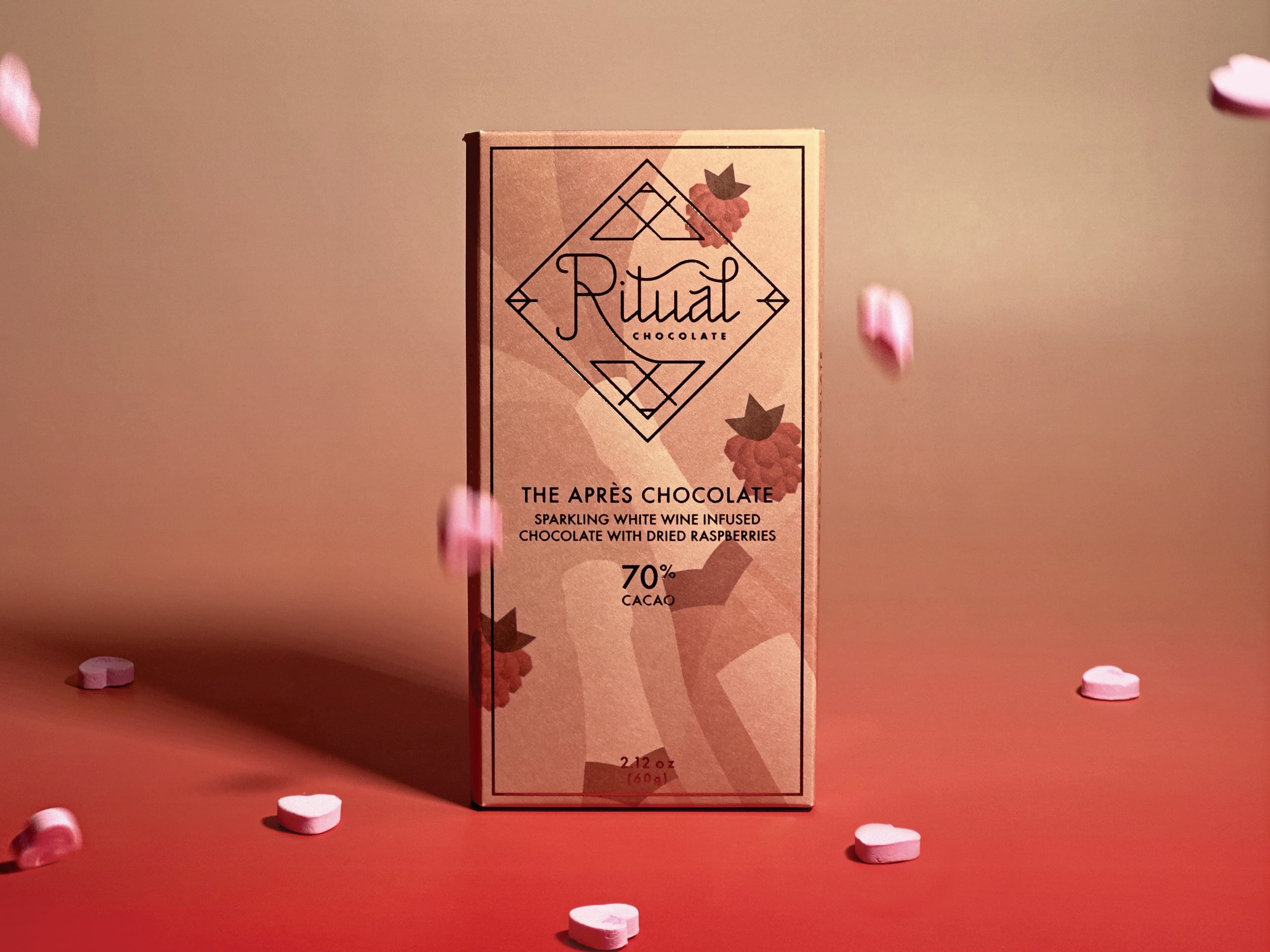 The Après Chocolate Sparkling White Wine Infused Chocolate With Dried Raspberries bar made by Ritual Chocolate in the United States on a gradient background with candy hearts